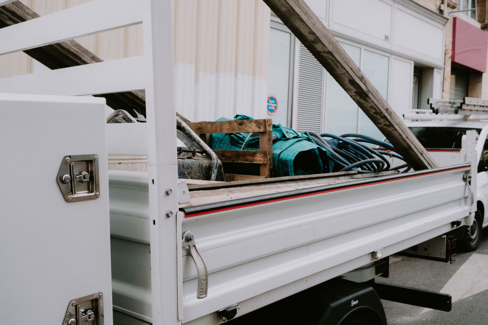 A white construction truck loaded with building materials and equipment parked by a building.